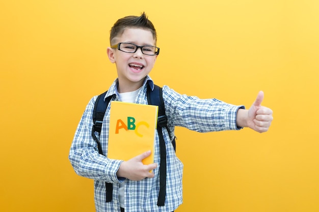 Kind jongen op een gele muur achtergrond geweldig idee gelukkig lachende schooljongen gaat terug naar school succes motivatie winnaar geniaal concept