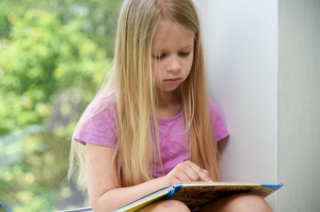 Kind leest 's middags een boek bij het raam.