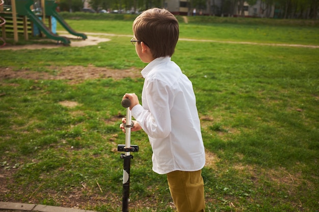 kind leren rijden een scooter in een stadspark Cute peuter jongen veiligheidshelm rijden op een roller