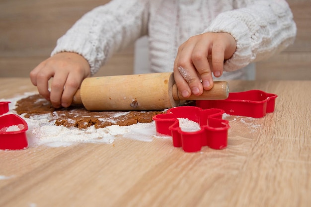 Kind maakt kerstkoekjes van peperkoekdeeg en koekjesmessen. Kerstkaartconcept.