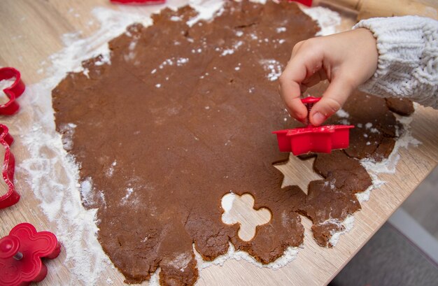 Kind maakt kerstkoekjes van peperkoekdeeg en koekjesmessen. Kerstkaartconcept.