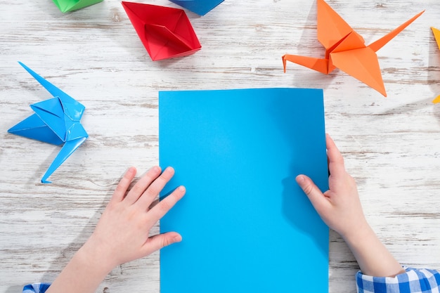 Kind maakt origami van gekleurd papier op een houten tafel