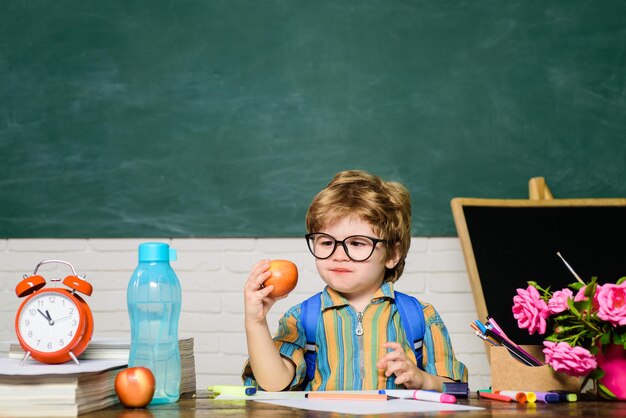 Kind maakt zich klaar voor school. Leraren dag. Schooljongen bij bord. Kind leert in de klas. Kleine jongen leerling aan balie met schoolbenodigdheden. Kinderschool. Leuke kindjongen in klaslokaal dichtbij bord.