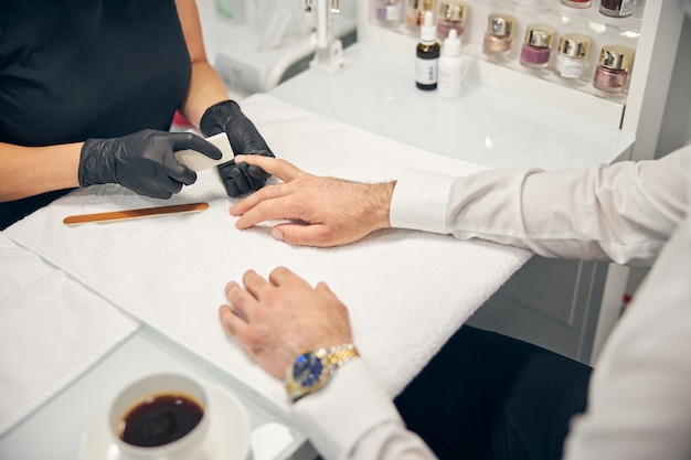 Kind male person sitting in semi position and putting hand on table for doing manicure