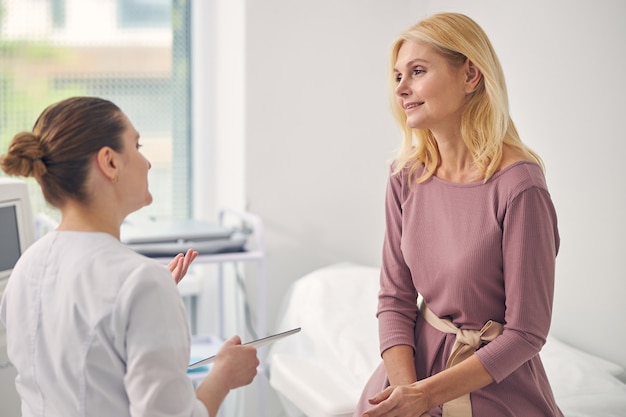 健康診断をしながら開業医の向かいに座っている親切な成熟した女性