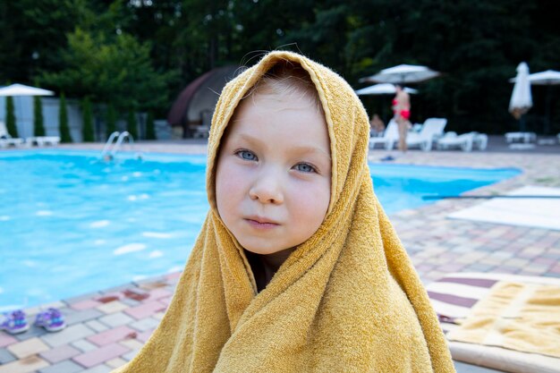 Kind meisje bedekt met een handdoek zit in de buurt van het zwembad