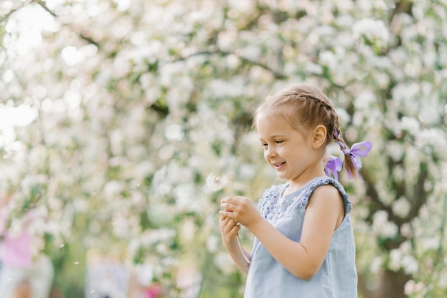 Kind meisje blaast op een paardebloem in een lente bloeiende tuin