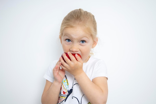 Kind meisje blond eet een appel op een witte achtergrond