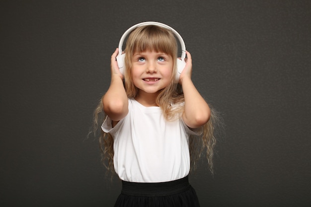 Kind meisje geniet van muziek in haar grote witte koptelefoon en glimlach.