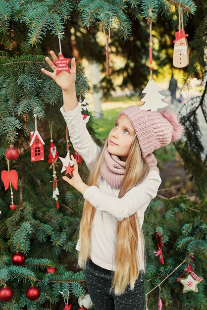 kind meisje in een hoed en sjaal in de buurt van de kerstboom