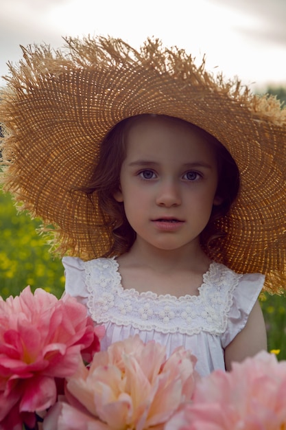 Kind meisje in een strooien hoed en een jurk met bloemen staat op een geel veld