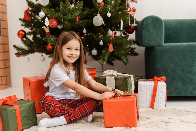 Foto kind meisje in pyjama opent een geschenk op kerstochtend gelukkig nieuwjaar