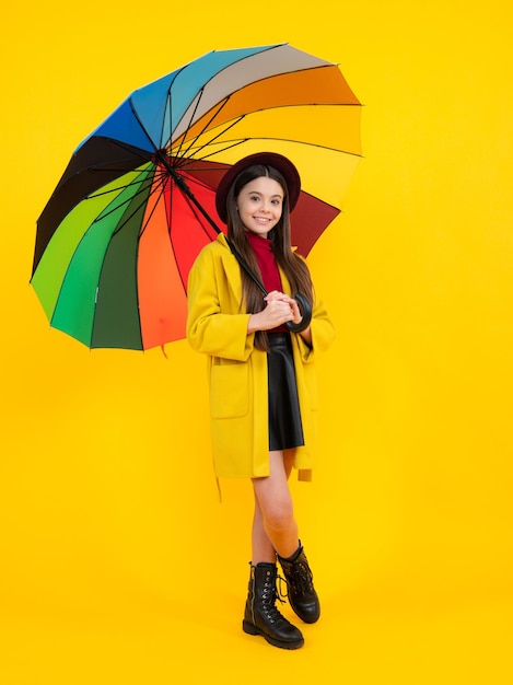 Kind meisje met regenboog paraplu in herfstweer geïsoleerd op gele achtergrond herfst kinderkleding glimlachend meisje in herfst jas gelukkig tiener portret volledige lengte