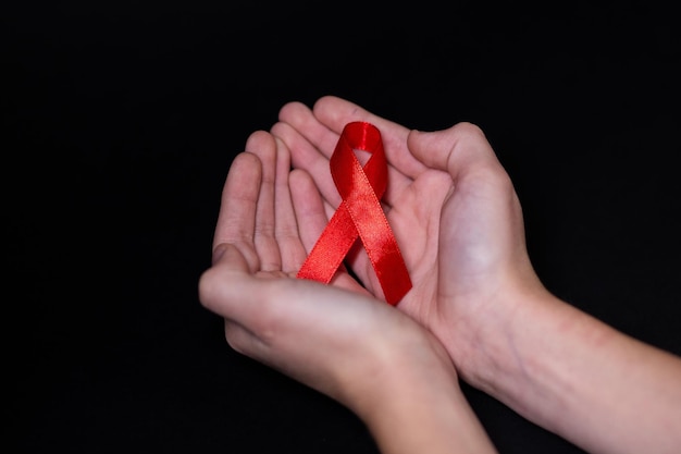 Kind menselijke handen houden rood lint symbool van aids op een zwarte achtergrond