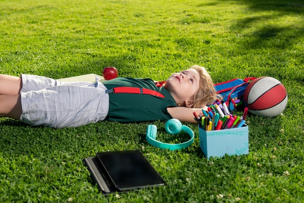 Kind met boek en taplet en rusten op het gras na school gelukkige jongen ontspannen op het gras