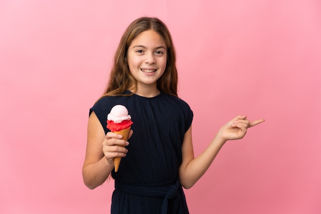 Kind met een cornetijs over geïsoleerde roze muur wijzende vinger naar de zijkant