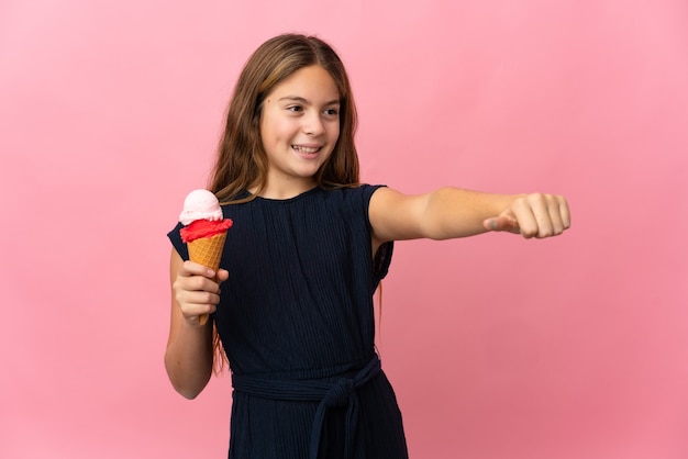 Kind met een cornetroomijs over geïsoleerde roze achtergrond die een duim omhoog gebaar geeft