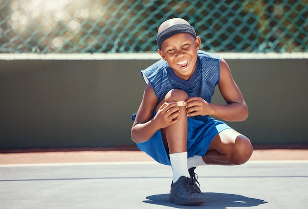 Kind met een pleister op een knieblessure van sporten buiten op een basketbalveld die zijn verband aanraakt jongen met een medische pleister per ongeluk gewond tijdens het trainen of oefenen voor een spel