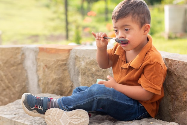 Kind met een verstandelijke beperking zittend op een bankje in een natuurpark op een zonnige dag die gelei eet