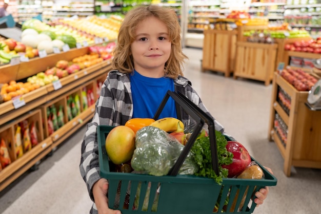 Kind met een winkelmandje vol groenten en fruit in een levensmiddelenwinkel die boodschappen doet