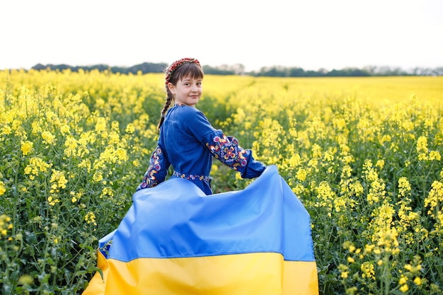 Foto kind met oekraïense vlag in koolzaadveld een meisje in een geborduurd shirt rent over het veld met de oekraïense vlag in haar handen