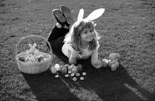 Kind met paaseieren en konijnenoren dat op het gras ligt en eieren schildert gelukkig paaseieren kindergezicht