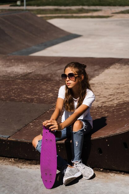 Kind met penny board Jong meisje tiener in glazen met skate board zittend op sport helling op skate speeltuin Extreme levensstijl Creatieve advertentie voor skate of penny board winkels of winkels