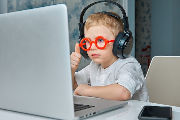 Kind met rode bril en koptelefoon heeft plezier bij het communiceren via videolink met behulp van een laptop