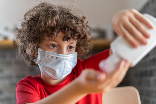 Kind met veiligheidsmasker dat ontsmettingsgel op zijn hand aanbrengt in een restaurant Heropening in de Covid19