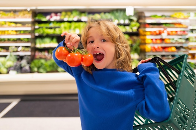 Kind met verse tomatengroenten Kind bij het winkelen in de supermarkt Kruidenierswinkel die goederen kiest Winkelen voor gezond