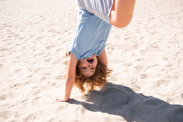 Kind ondersteboven springen op zand grappige kinderen emoties buiten close-up portret van een schattig klein kind