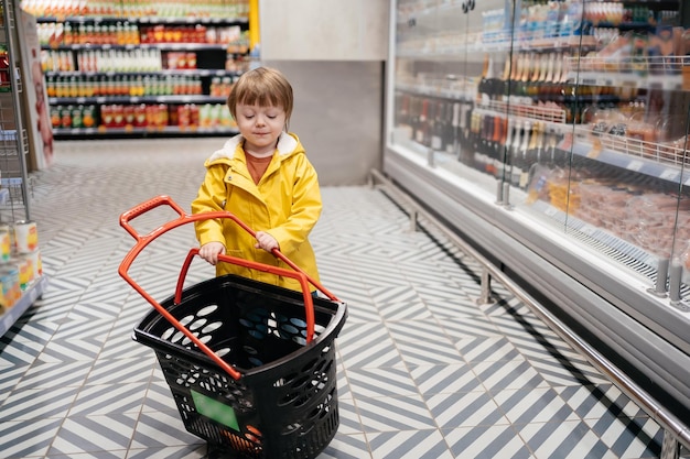 Kind op de markt met een boodschappenwagentje in een gele jas en spijkerbroek