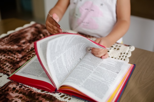 Kind op tafel leest de bijbel en bladert erin