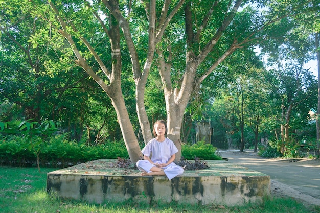 kind op witte kleding, oefen zittend Meditatie onder de grote boom met gemoedsrust