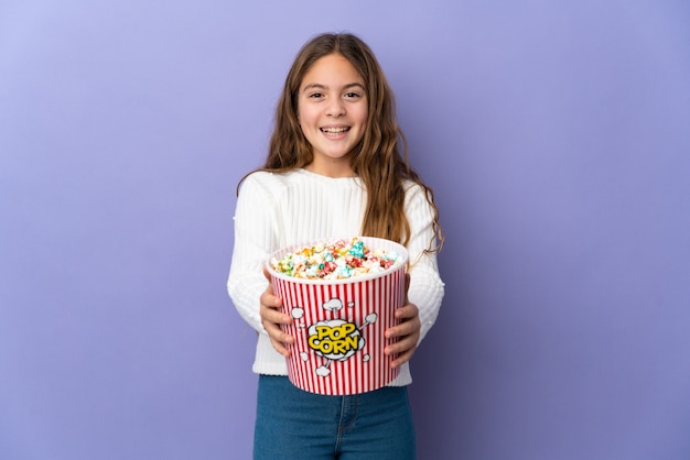 Kind over geïsoleerde paarse achtergrond met een grote emmer popcorn