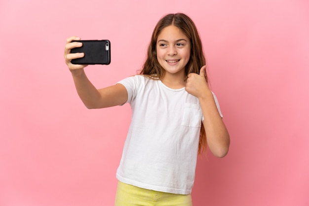 Kind over geïsoleerde roze achtergrond die een selfie maakt met mobiele telefoon