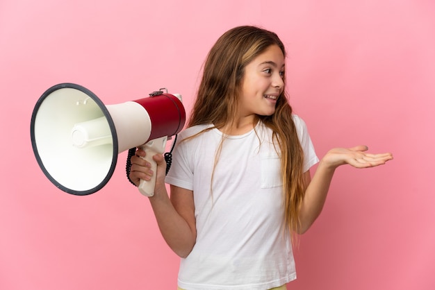 Kind over geïsoleerde roze achtergrond met een megafoon en met verrassende gezichtsuitdrukking