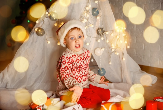 Kind pakt cadeautjes uit onder de kerstboom schattige jongen met een kerstmuts