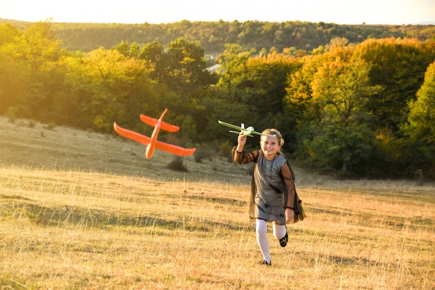 Kind piloot vlieger met vliegtuig droomt van reizen in de zomer in de natuur bij zonsondergang kinderen lopen gelukkig samen tijdens mooi zonnig weer in het park