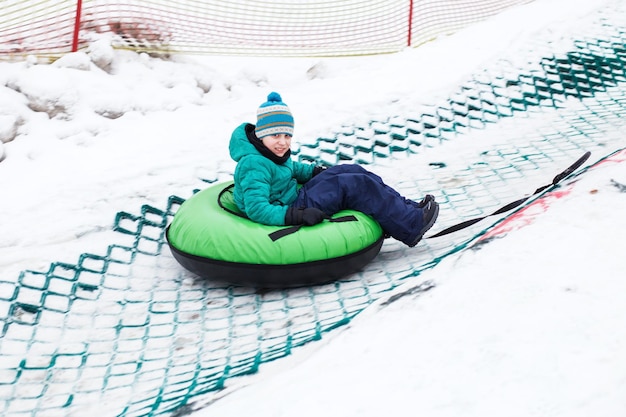 Kind plezier op sneeuwbuis Jongen rijdt op een slang Winterentertainmentkind glijdt bergafwaarts