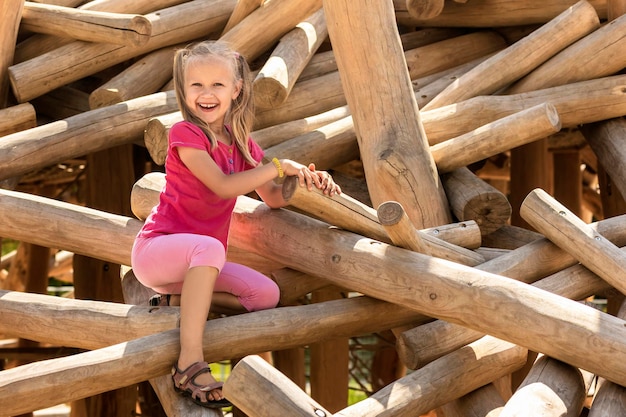 Kind plezier op speelplaats Klein kind klimmen op houten logboeken van speeltoestellen