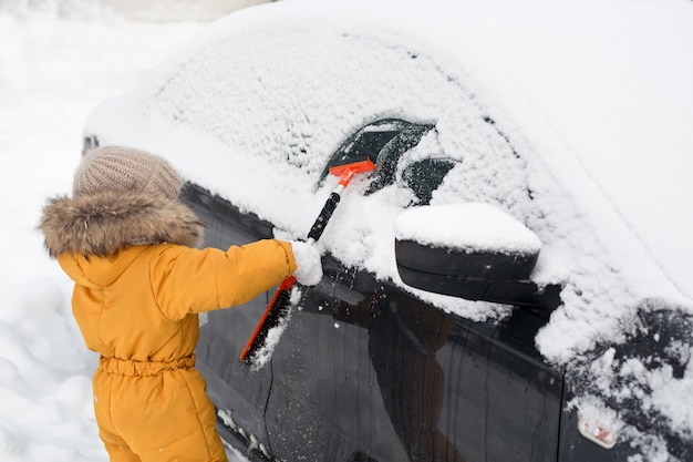 Kind poetsen sneeuw van auto na storm