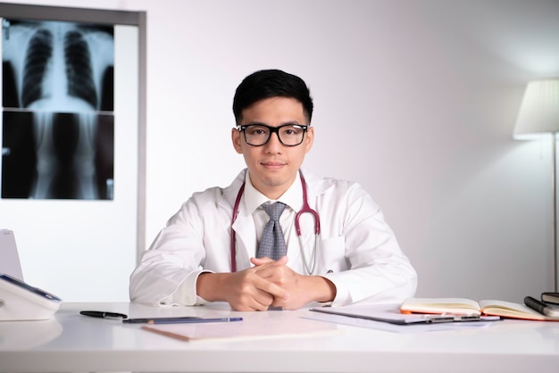 Kind and polite young Asian medical doctor orthopaedic surgeon wearing stethoscope with laptop