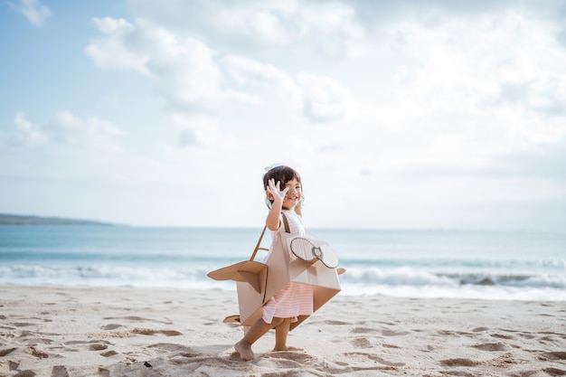 Kind rent op het strand spelen met kartonnen speelgoedvliegtuig