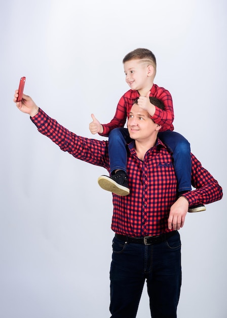 Kind rijdt op vaders schouders Geluk als vader van jongen Plezier hebben Vaderdag Vader voorbeeld van nobele mens Vader zoontje rode shirts familie look outfit Selfie maken met zoon