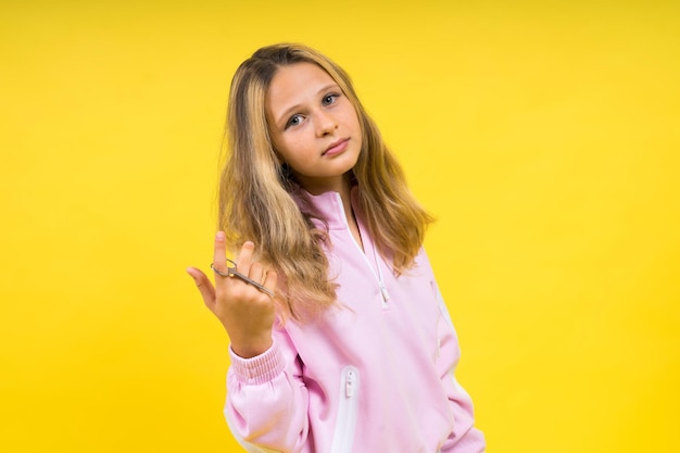 Kind schattige meisjeskapper die lang blond haar knipt met een metalen schaar op geel