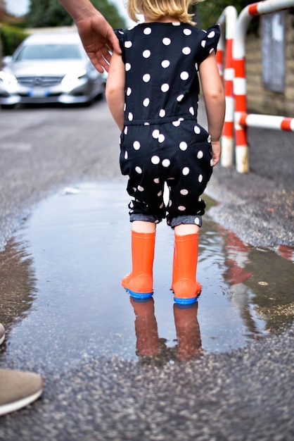 kind speelt in een plas in rubberen laarzen na de zomerregen