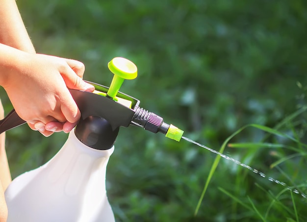 Kind speelt met een waternevelcontainer Bloembed water geven op een warme zomerdag buitenshuis