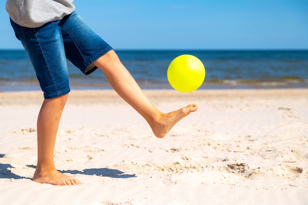 Kind spelen met gele strandbal op het zand door het zeewater op een zonnige dag.