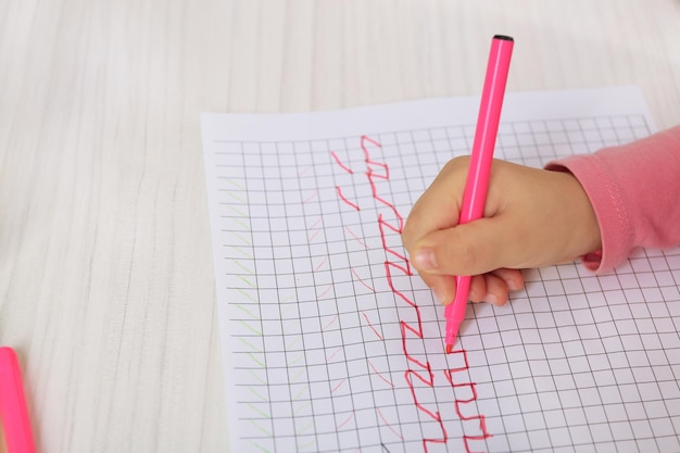 Kind tekent met roze viltpen op papier close-up